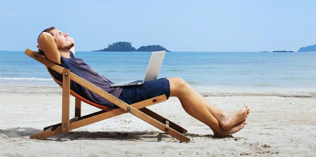 Man relaxing on a beach chair with a laptop, enjoying a leisurely moment by the seaside.