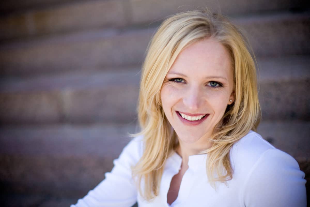 A smiling woman with blonde hair sitting on steps.