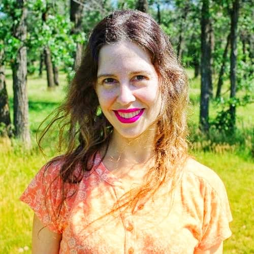 A smiling woman with bright lipstick enjoys a sunny day in a lush green park.