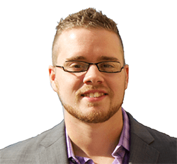 A confident young man with stylish glasses and a neatly trimmed beard, wearing a smart grey suit jacket over a purple shirt, smiling against a clear background.