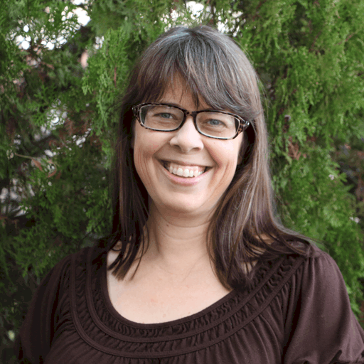 A smiling woman with glasses in front of a green leafy background.