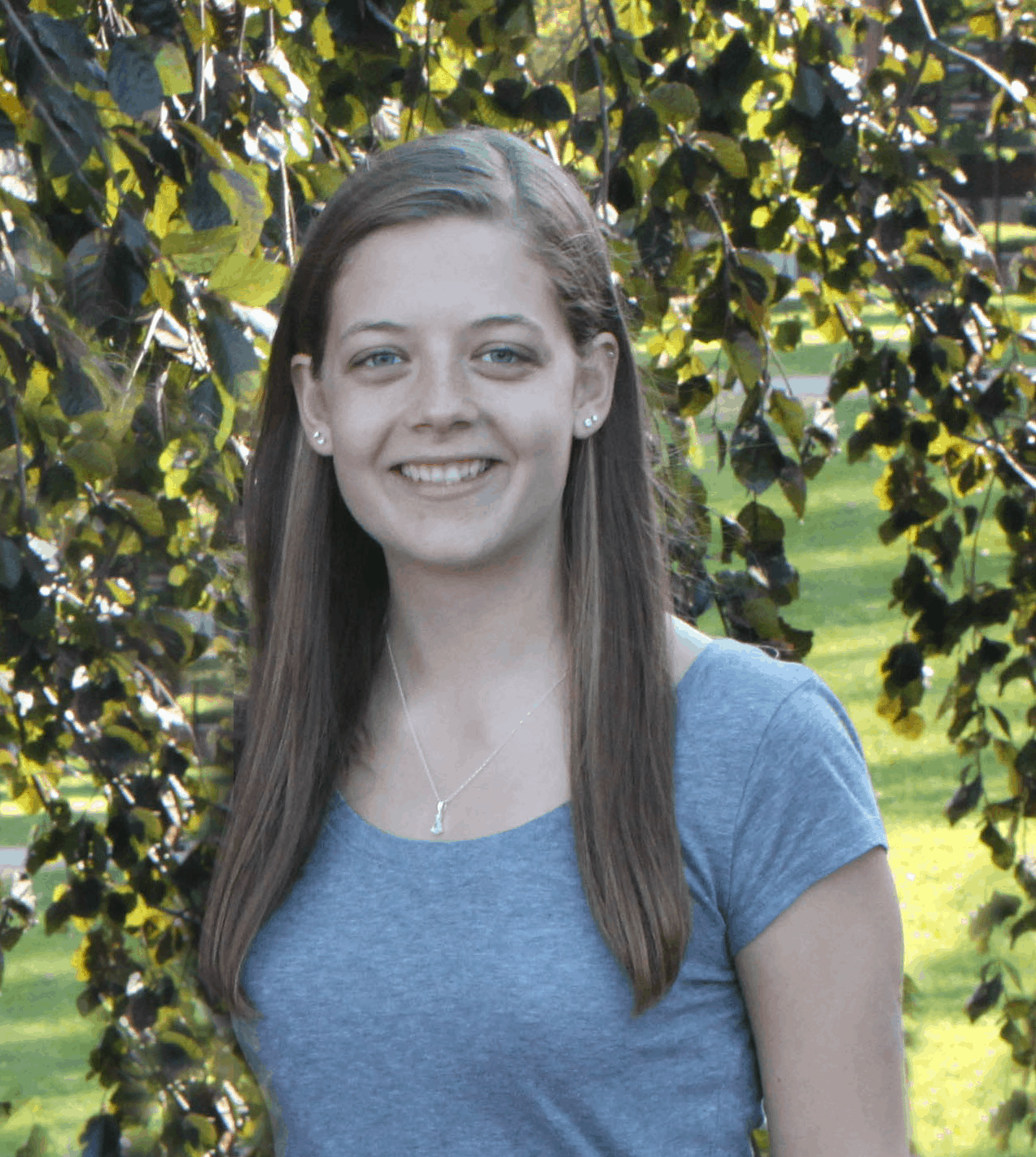A smiling young woman standing in front of green foliage.