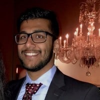 A man in a suit and tie smiling in front of an elegant chandelier.