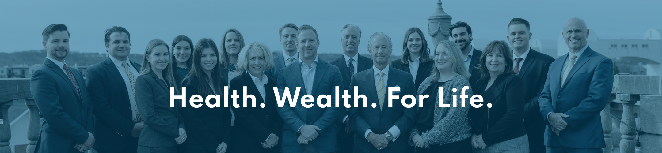 A group of professionally dressed people standing together outdoors, smiling at the camera, with the words 