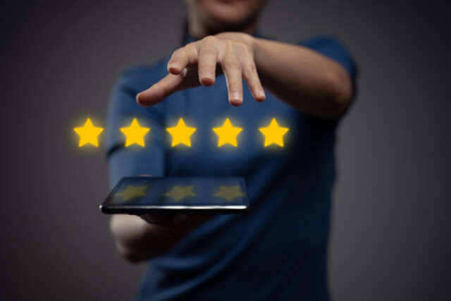 A person holding a tablet extends their hand toward five glowing yellow stars, representing a five-star rating, with a dark background.