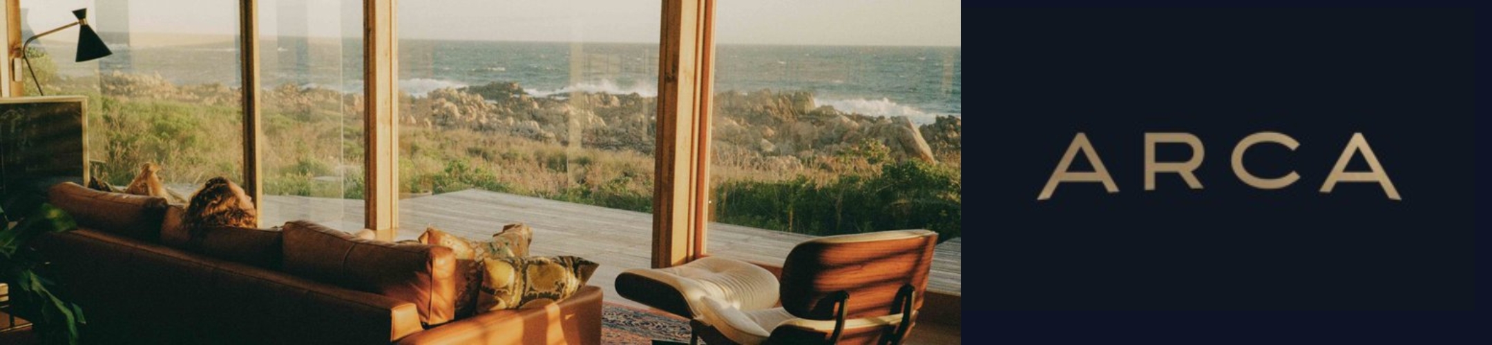 A cozy living room with leather sofas and a modern chair overlooks a scenic ocean view through large glass windows. Next to it, the word 